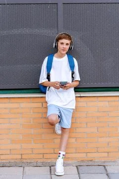 Boy with headphones looking at camera while holding a mobile phone outdoors. Foto stock