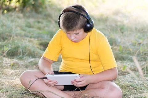 Boy in headphones looking tablet computer on the nature Stock Photos