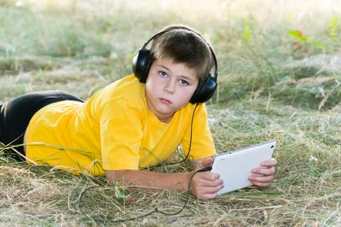 Boy in headphones looking tablet computer on the nature Stock Photos