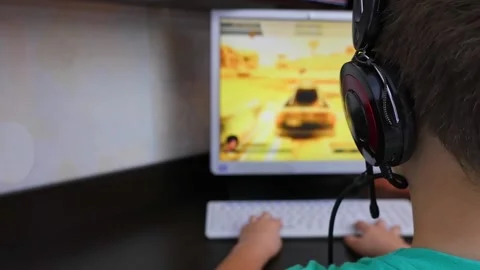 A boy with headphones is playing a computer game in front of a personal compu Stock Footage 168486614