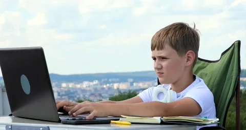 The boy in headphones studies at the computer, makes notes in the notebook an Stock Footage 136541864