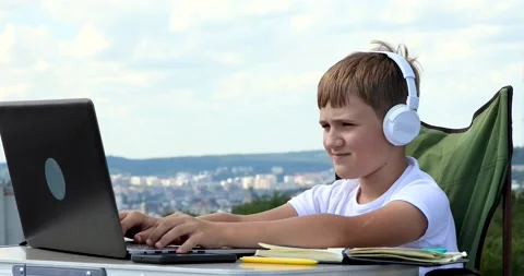 The boy in headphones studies at the computer, makes notes in the notebook an Stock Footage 136541915