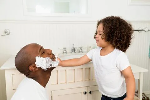 Boy helping father shave in bathroom Stock Photos