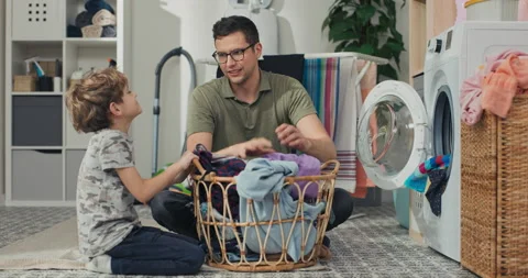 The boy helps his dad put dirty clothes in the washing machine, they take things 库存影片 200840061