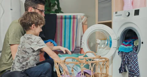 The boy helps his dad put dirty clothes in the washing machine, they take things 库存影片 200850043