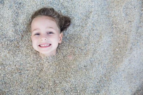 Boy hidden in the sand on the beach Stock Photos