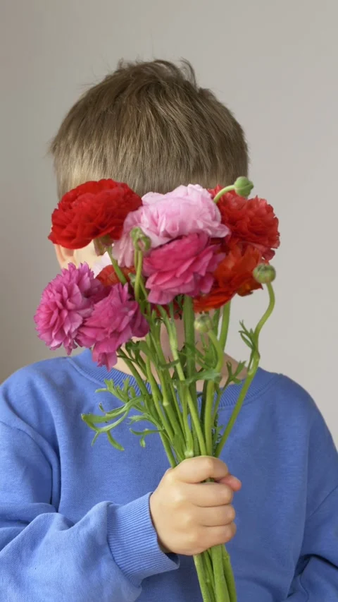 Boy hides behind large bouquet of ranunculus flowers and then peeks out smiling 스톡 동영상 335653413