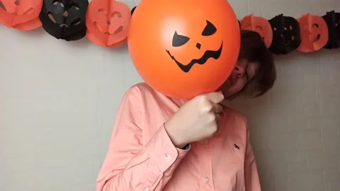 A boy hiding his face behind orange pumpkins balloon Stock Footage 141038681