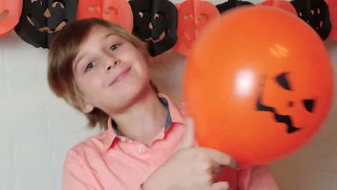 A boy hiding his face behind orange balloon, Halloween at home Stock Footage 141038824