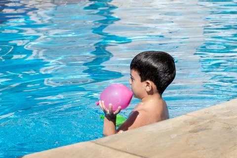 Boy on his back inside the pool holding a pink water balloon. Stock Photos