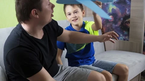 A boy with his dad sitting on the couch playing with a blue airplane. the plane Stock Footage 168486374