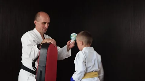 Boy hits punches on a large exercise machine in motion, trainer helps to refresh Stock Footage 303434110