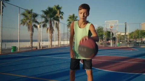 Boy hitting a basketball ball, practicing on a court and looking at the camera Stock Footage 207120438