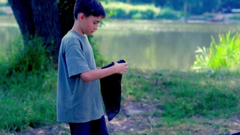 Boy holding black trash bag while standing on riverbank Stockbeeldmateriaal 340465108