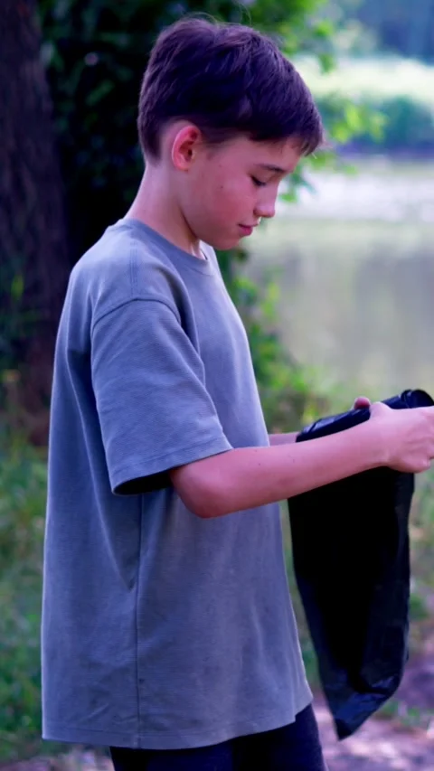 Boy holding black trash bag while standing on riverbank Stock Footage 340577874