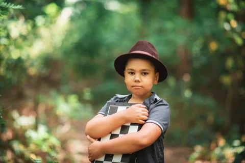 Boy holding a folded chessboard in a forest Foto stock