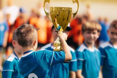 Boy holding golden trophy and celebrating sport success with team Stock Photos
