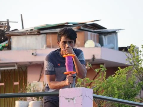 A boy holding the kite thread while standing on the rooftop. Stock Photos