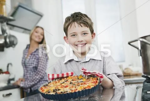Boy holding pizza with mother in background Stock Photos