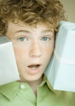 Boy holding up presents on either side of face Stock Photos