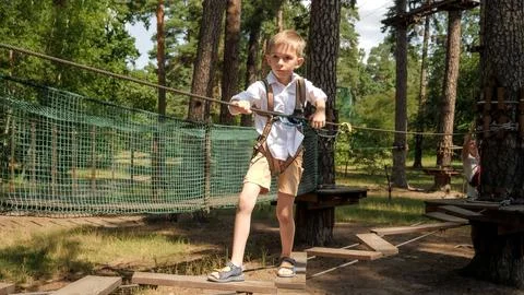Boy holding rope while walking over wobbly wooden bridge at outdoor adventu.. Stock Photos