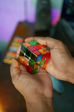 A boy is holding a Rubik's Cube with a table and speakers on the background Stock Photos
