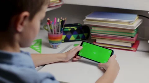 Boy holding a smartphone with a green screen at home, scrolling touching screen Stock Footage 166312914