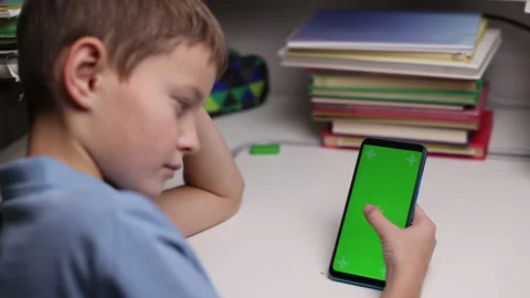 Boy holding a smartphone with a green screen at home, scrolling touching screen Stock Footage 166730701