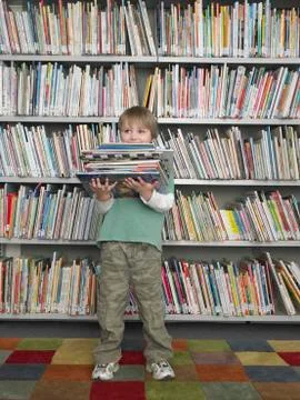 Boy Holding Stack Of Books In Library Stockfoto's