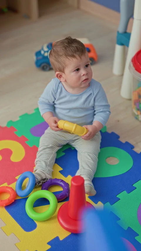 Boy holding yellow ring toy sitting on colorful foam mat in a building play.. Stock Footage 337388744