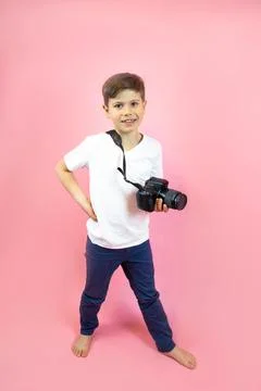 A boy holds a camera in his hands, dressed in a white t-shirt and blue jeans on Stock Photos