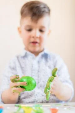 A boy holds a green Easter egg in his hands stained with paint on a white bac Stock Photos