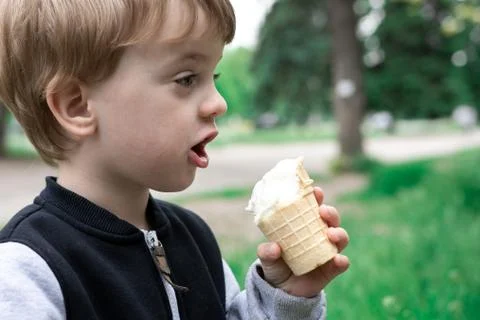Boy holds in hand and eats ice cream in a summer park. Stock Photos