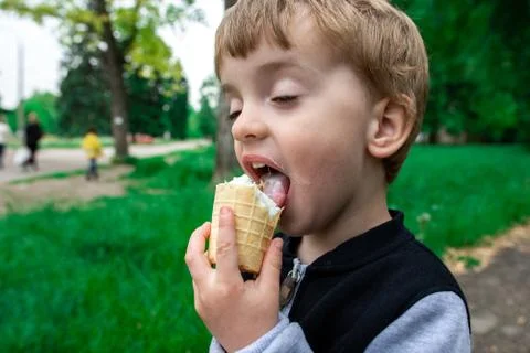 Boy holds in hand and eats ice cream in a summer park. Stock Photos