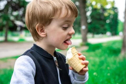 Boy holds in hand and eats ice cream in a summer park. Stock Photos