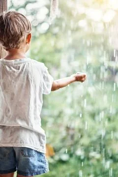 Boy holds hand under falling down rain drops on terrace Foto stock