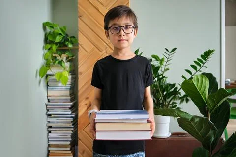 A boy holds a stack of books against the background home library. Stock Photos