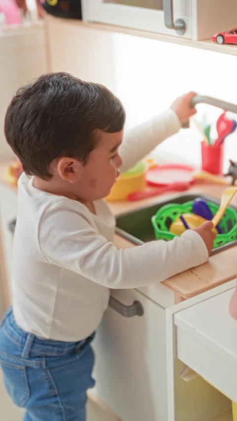 Boy holds a yellow fork at a toy sink beside a play kitchen in a building p.. Stock Footage 339187683
