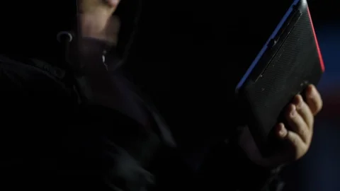 Boy in the hood in the evening playing on the tablet in the park Stock Footage 96874797