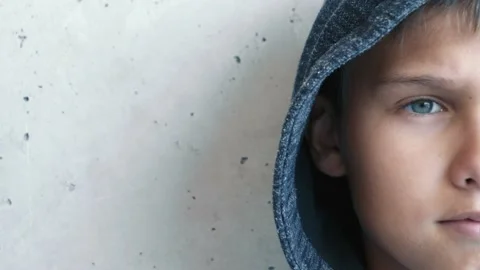 Boy in hood looking directly to camera. Half face. Child near grunge gray wall Stock-Footage 131914757