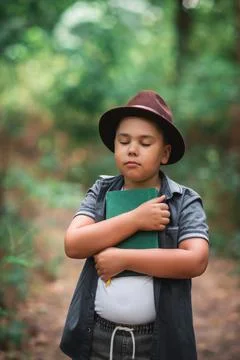 Boy hugging a book vertically in a green forest. Stock Photos