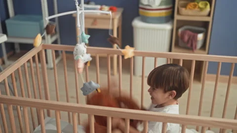 Boy hugging a plush monkey and reaching for a hanging mobile while seated i.. Stock Footage 339248055