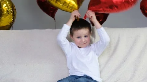 Boy is indulging with a red and gold heart-shaped balloon on a light sofa Stock Footage 146163994