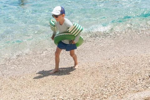Boy with inflatable ring on pebble beach 写真素材