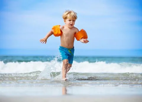Boy in inflatable shoulder straps run from the ocean waves Stock Photos