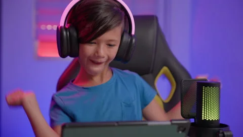 Boy Influencer Raises Hand While Looking at Tablet in Gaming Chair Stock Footage 345961942