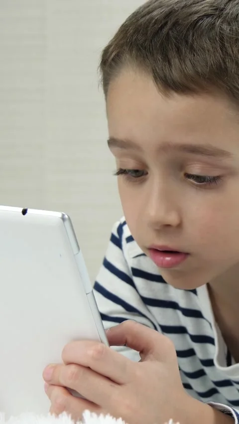 Boy interacts with tablet using touchscreen while resting indoors. Vertical Stock Footage 348230952