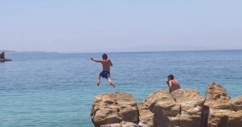 Boy on island having fun jumping off rock and landing into sea water Stock Footage 148243793