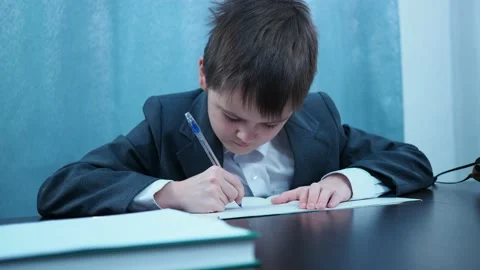 A boy in a jacket and shirt writes in a notebook at the Desk Stock Footage 144179624
