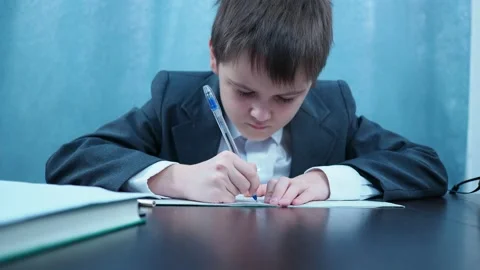 A boy in a jacket and shirt writes in a notebook at the Desk Stock Footage 144179673